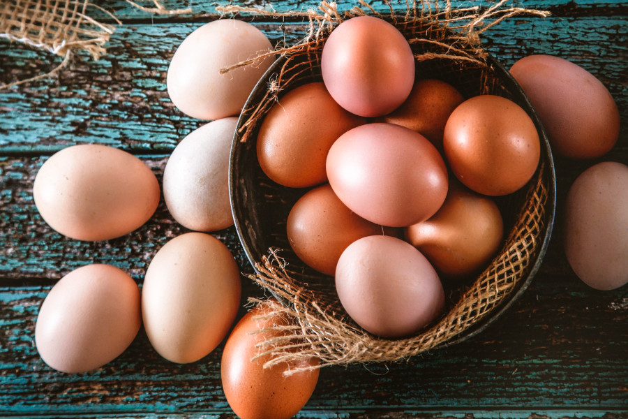 Braune Bio-Eier in und um eine Schale auf rustikalem Holztisch.